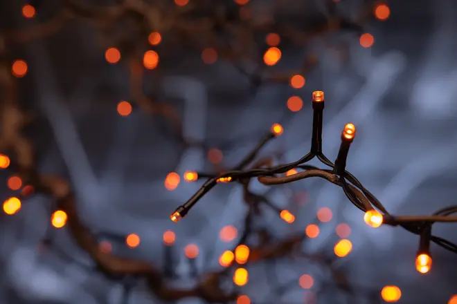 Slinga med orange LED-lampor på mörka sladdar, lyser varmt. Passar för dekoration inomhus eller utomhus. Bakgrunden är suddig.