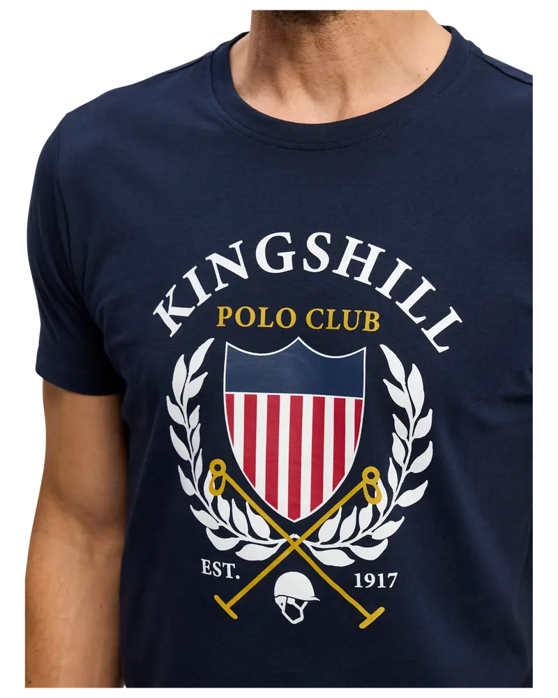 Mörkblå t-shirt med texten "Kingshill Polo Club", sköld med röda och vita ränder, lagerkrans, korsade poloklubbor och hjälm. Grundad 1917.