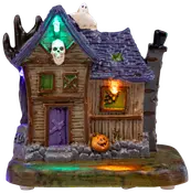 Keramikhus i spökstil med lila tak, brädade fönster, färgade lampor, ett spöke på taket och en pumpa vid basen. Perfekt för Halloween.