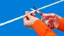 Gennemsigtige sakse klipper en fleksibel LED-lysbånd, holdt af en person med orange ærme, mod blå baggrund. Båndet har små, jævnt fordelte LED'er.