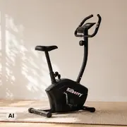Sort motionscykel med opret sæde, justerbart styr og digital konsol, vist på et tæppe foran en lys væg.