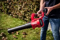 Röd och svart SKIL batteridriven lövblås med ergonomiskt handtag, lätt design och lång munstycke. Perfekt för att rensa löv och skräp i trädgården.