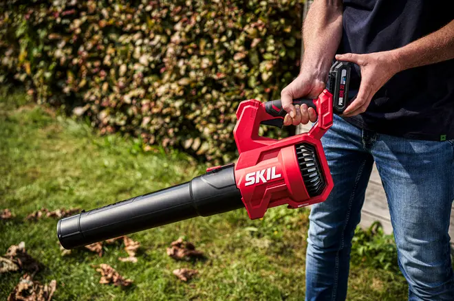 Rød og sort SKIL batteridrevet løvblæser med ergonomisk håndtag, letvægtsdesign og lang dyse. Ideel til effektiv fjernelse af blade og snavs i haven.