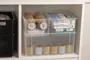 Gennemsigtige plastikopbevaringskasser på en hylde, indeholdende ruller med tape og pakkede medicinske forsyninger. Kasserne er stablebare og giver nemt overblik over indholdet.