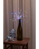 Vinflaska med flerfärgade LED-ljusslingor arrangerade som fyrverkerier, används som dekorativ mittpunkt. Glasburk med små discobollar och stjärnformade dekorationer intill.