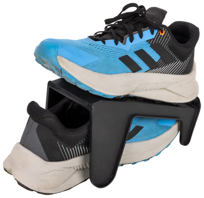 Blå og sorte sportssko placeret på en sort plastik sko-organisator, som holder én sko ovenover den anden for at spare plads og holde skoene organiseret.