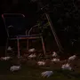 Rusten metalstol og skovl i en have ved skumring, omgivet af flere hvide plastikhandsker spredt på græsset og jorden, hvilket skaber en mystisk stemning.