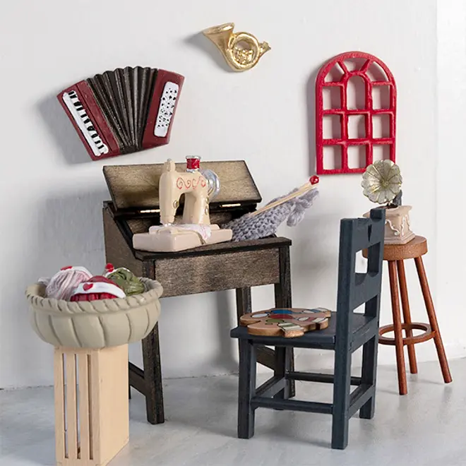 Miniature håndværksrum med symaskine, garnkurv, klaver, stol, skammel, grammofon, vægmonteret harmonika, horn og rødt vindue. Farverig og detaljeret, perfekt til dukkehuse.