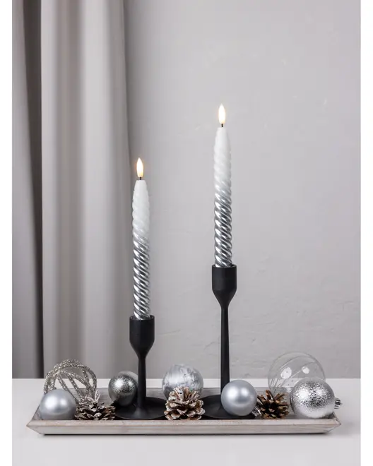 Dekorativt sæt med to spiralformede hvide og sølvfarvede stearinlys i sorte stager, arrangeret på bakke med sølvkugler og kogler, ideelt til festlig borddækning.