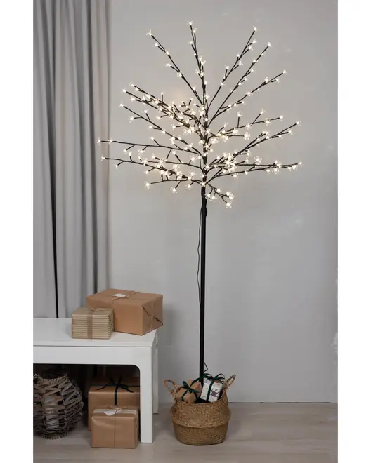 Konstgjort träd med svarta grenar, dekorerat med många små vita LED-lampor, placerat i en flätad korg. Modern dekorbelysning för inomhusbruk.