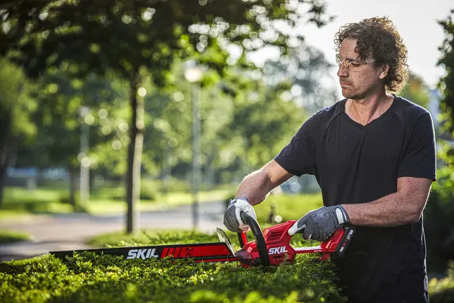 Röd och svart SKIL häcksax med ergonomiskt handtag, långt skärblad och skydd. Perfekt för att trimma häckar och buskar. Lätt och enkel att använda.