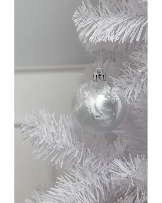 Sølvfarvet julekugle i glas med marmoreret finish, hængende på en hvid kunstig juletræsgren. Kuglen har blank, reflekterende overflade og metalophæng.