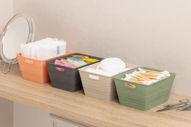 Sæt med fire rektangulære plastkasser i orange, sort, beige og grøn, hver med forskellige badeværelsesartikler som vatrondeller, vatpinde, servietter og små poser. Håndtag på siderne.