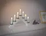 Hvid elektrisk lysestage med syv LED-lys, hver pyntet med små grønne grangrene, arrangeret i en buet form. Velegnet til jule- eller festdekoration.