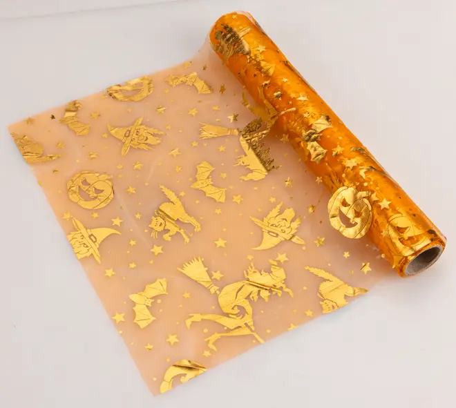 Orange transparent presentpapper med gyllene Halloween-motiv som häxor, fladdermöss, pumpor, katter och stjärnor. Perfekt för festlig inslagning eller dekoration.