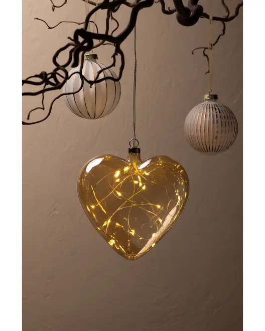 Hjerteformet glaspynt med varme LED-lyskæder indeni, hængende fra en gren. To runde, stribede glas kugler hænger også tæt på. Perfekt til festlig eller romantisk dekoration.