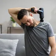 Handhållen elektrisk massagepistol med ergonomiskt handtag och runt munstycke, används för muskelavslappning och djupvävnadsmassage, visas på nacke och axel.