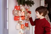 Hængende julekalender med små røde, hvide og stribede gaveæsker ophængt i snore under gran.