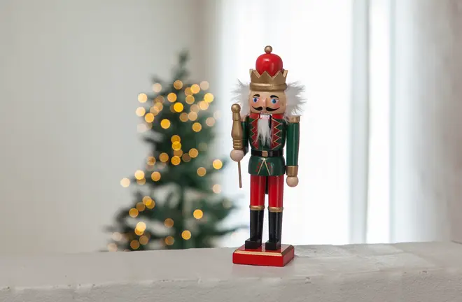 Trä-nötknäppare med röd, grön och guld uniform, vitt skägg och krona. Står på röd bas, håller en spira. Klassisk juldekoration.