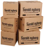 Stak af seks brune flytte- og opbevaringskasser i pap med håndtag, 'harald nyborg' logo og hjemmeside trykt på siden. Velegnet til opbevaring og flytning.