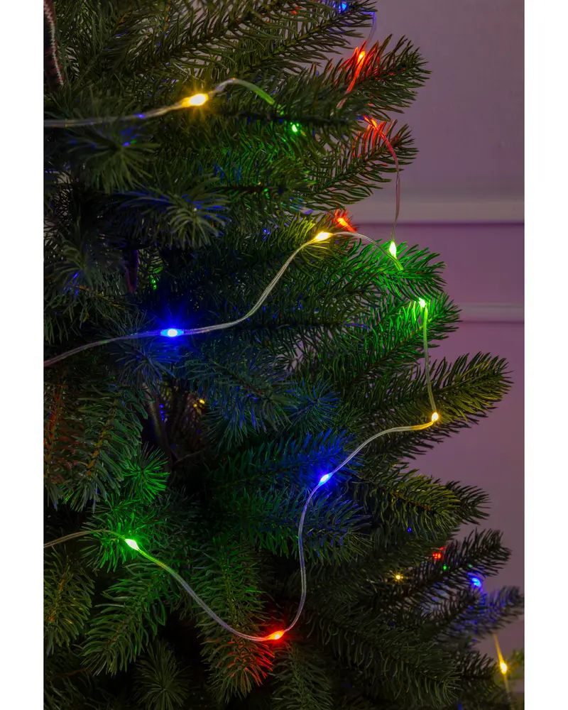 A close-up view of a green artificial Christmas tree decorated with a string of multicolored LED lights. The lights are small and evenly spaced along a thin, transparent wire, emitting bright colors including blue, red, yellow, and green. The tree branches are dense and realistic, and the lights create a festive glow against the dark green needles.