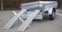 Enkeltakslet trailer med metalsider, åbent lad og to aftagelige læsseramper. Robust hjul, bagreflekser og rummeligt lad til transport af udstyr eller varer.