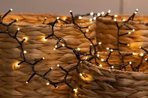Close-up of a string of small, warm white LED lights with a black wire, draped over woven, natural-colored baskets. The lights are evenly spaced and emit a soft, cozy glow, highlighting the texture of the baskets.