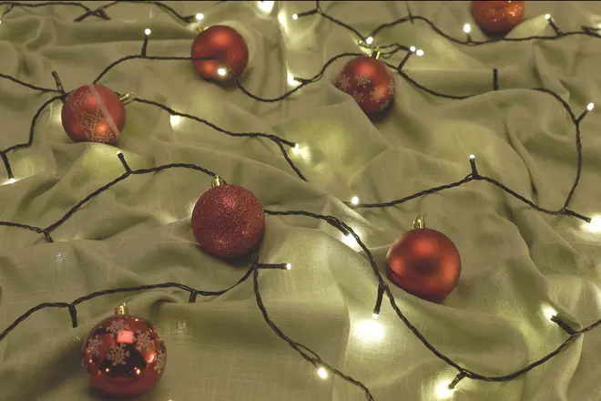 Varme hvide lyskæder med sort ledning og røde julekugler på draperet beige stof.