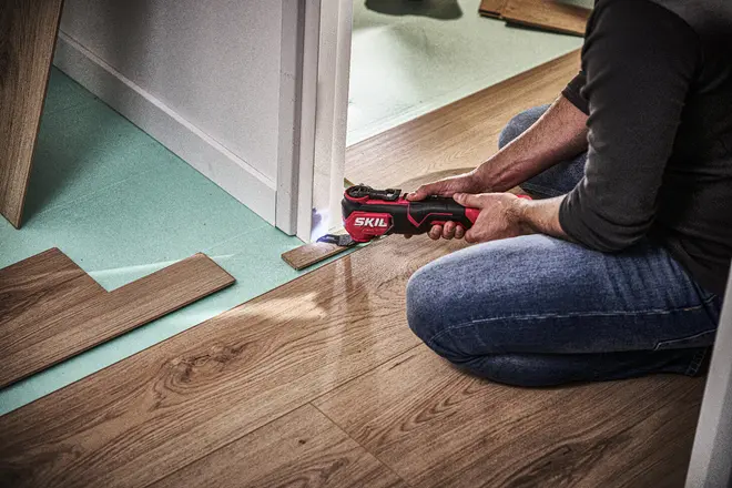 Trådløst SKIL multiværktøj med ergonomisk greb, bruges til præcis skæring af dørkarme og gulv under installation. Værktøjet har LED-lys og er velegnet til gør-det-selv-opgaver.