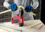 Rød og sort SKIL varmepistol med sidehåndtag, brugt til at varme og bøje plastslanger på en arbejdsbænk.