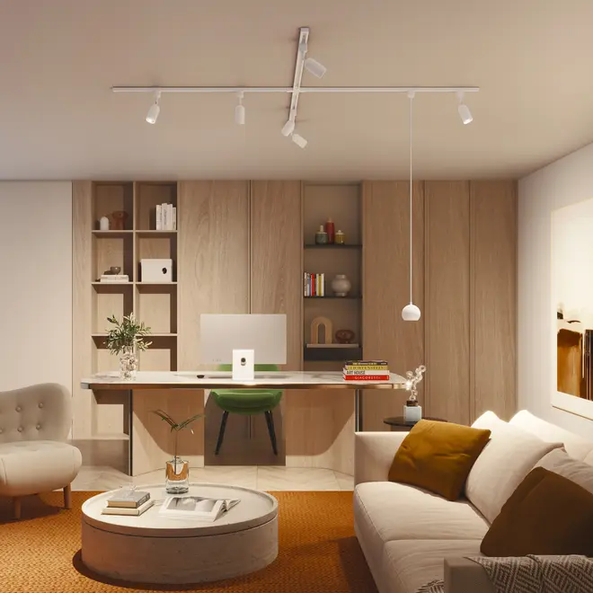 Moderne hjemmekontor med indbyggede træhylder, hvidt skrivebord, grøn stol, beige sofa med brune puder, rundt sofabord og loftsskinnebelysning. Minimalistisk og hyggeligt design.