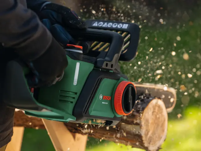 Bosch batteridrevet kædesav med ergonomisk håndtag, grøn og sort krop, sikkerhedsskærm og synligt batterirum, designet til effektiv træskæring og udendørs brug.