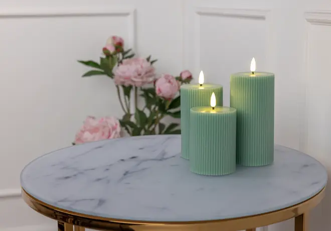 Set med tre gröna, räfflade blockljus med realistiska LED-lågor, placerade på ett runt marmorbord. Elegant, modern design för heminredning eller speciella tillfällen.
