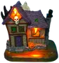 Halloween-dekoration: spökhus med lila tak, orange lampor, spökfigur på taket, pumpa, brädade fönster och stensockel. Tillverkad i målad resin, för bordsdekoration.