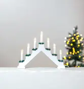 Hvid elektrisk lysestage i træ med syv LED-lys, hver pyntet med grønne kranse. Velegnet til vindueskarme eller juleudsmykning. Ledning ses ved bunden.