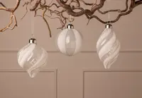 Set med tre vita julgransprydnader i glas med silverglitter, runda och spiralformade, varje med silverfäste och upphängningsögla för enkel dekoration.