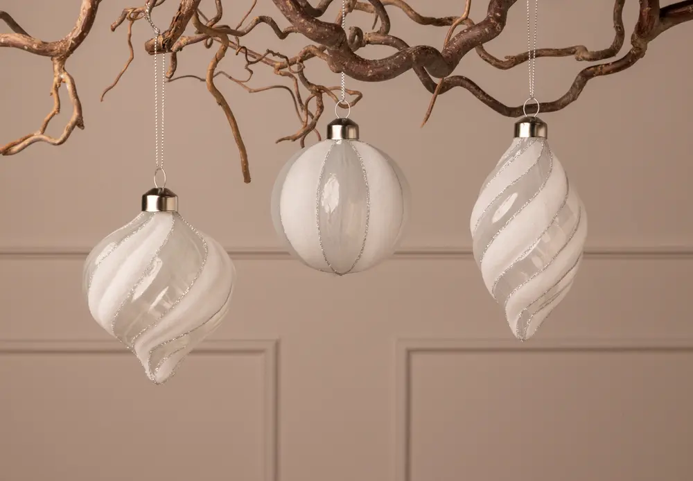 Set med tre vita julgransprydnader i glas med silverglitter, runda och spiralformade, varje med silverfäste och upphängningsögla för enkel dekoration.