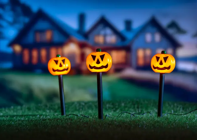 Set med tre Halloween-trädgårdslampor med leende pumpahuvuden på svarta stolpar, sammankopplade med sladd, passar utomhusdekoration.