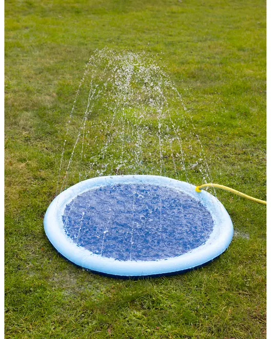 Rund blå vandlegeplads med vandstråler, der sprøjter op fra kanten. Tilsluttet en gul haveslange, ideel til udendørs leg på græs.