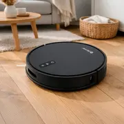 Sort robotstøvsuger på trægulv i en stue, med rundt lavprofildesign og topmonterede kontrolknapper.