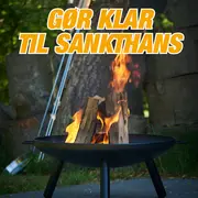 Rund sort bålfad med tre ben, brændende træstykker indeni. Velegnet til udendørs brug, perfekt til sankthans eller hygge. Robust metal, moderne design, nem at flytte.