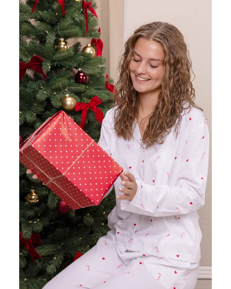 Vitt pyjamaset med små röda polkagrisar och hjärtan, långärmad skjorta med knappar och matchande byxor. Mjukt bomullstyg, perfekt för mysiga julkvällar eller sömn.