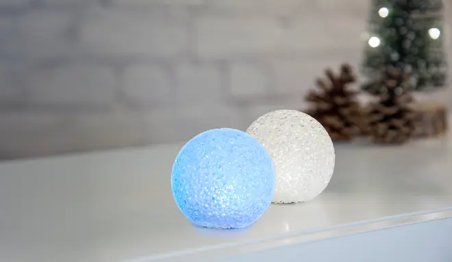 Sæt med to LED-glas kugler med tekstur, én lyser blå og én hvid. Dekorative, batteridrevne, perfekte til jul eller stemningsbelysning. Placeret på hvid overflade.