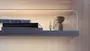 Moderne træhylde med indbygget LED-lys, indeholder stakke af bøger og dekorative glas- og keramikgenstande, monteret mod en lys trævæg for et minimalistisk udtryk.