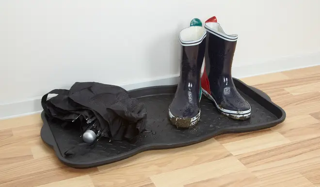 Svart plastbricka för skor med ett par leriga stövlar och ett vått, hopfällt paraply. Brickan skyddar golvet från smuts och vatten, perfekt i hallen.