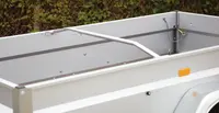 Öppen släpvagn med höga metallsidor, tvärgående stödstång och ljusgrå finish. Sidoreflexer och synliga fästpunkter inuti.