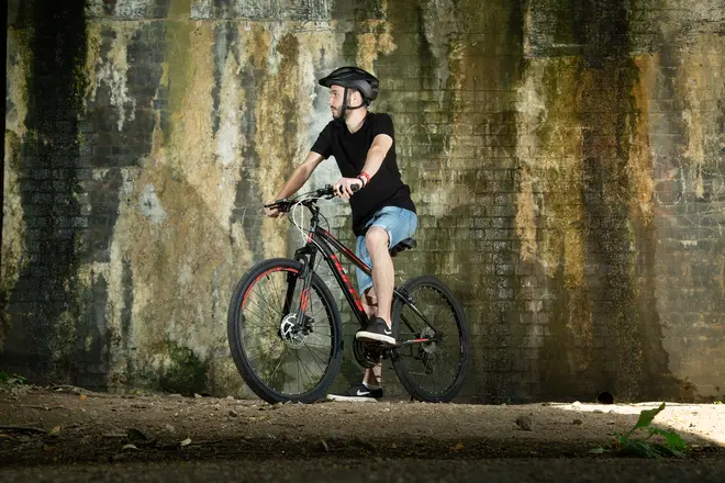 Mountainbike med affjedring foran, skivebremser og grove dæk. Sort stel med røde detaljer, fladt styr, velegnet til terræn- eller sticykling.