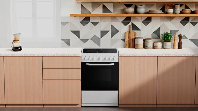 Fristående svart och silver elektrisk spis med fyra plattor, vred och ugn. Passar mellan ljusa träskåp, modern geometrisk kakel och vit bänkskiva.