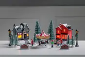 Miniatyr-julby med två upplysta hus, karusell, snötäckta granar, lyktstolpar och små figurer. Skapar en mysig och festlig vinterkänsla för dekoration.
