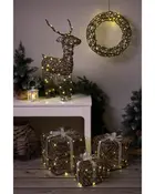 Dekorationsset med flätad ren, krans och paket, alla insvepta i varmvita LED-ljusslingor. Perfekt för inomhus juldekoration. Naturligt brun färg och vita band.